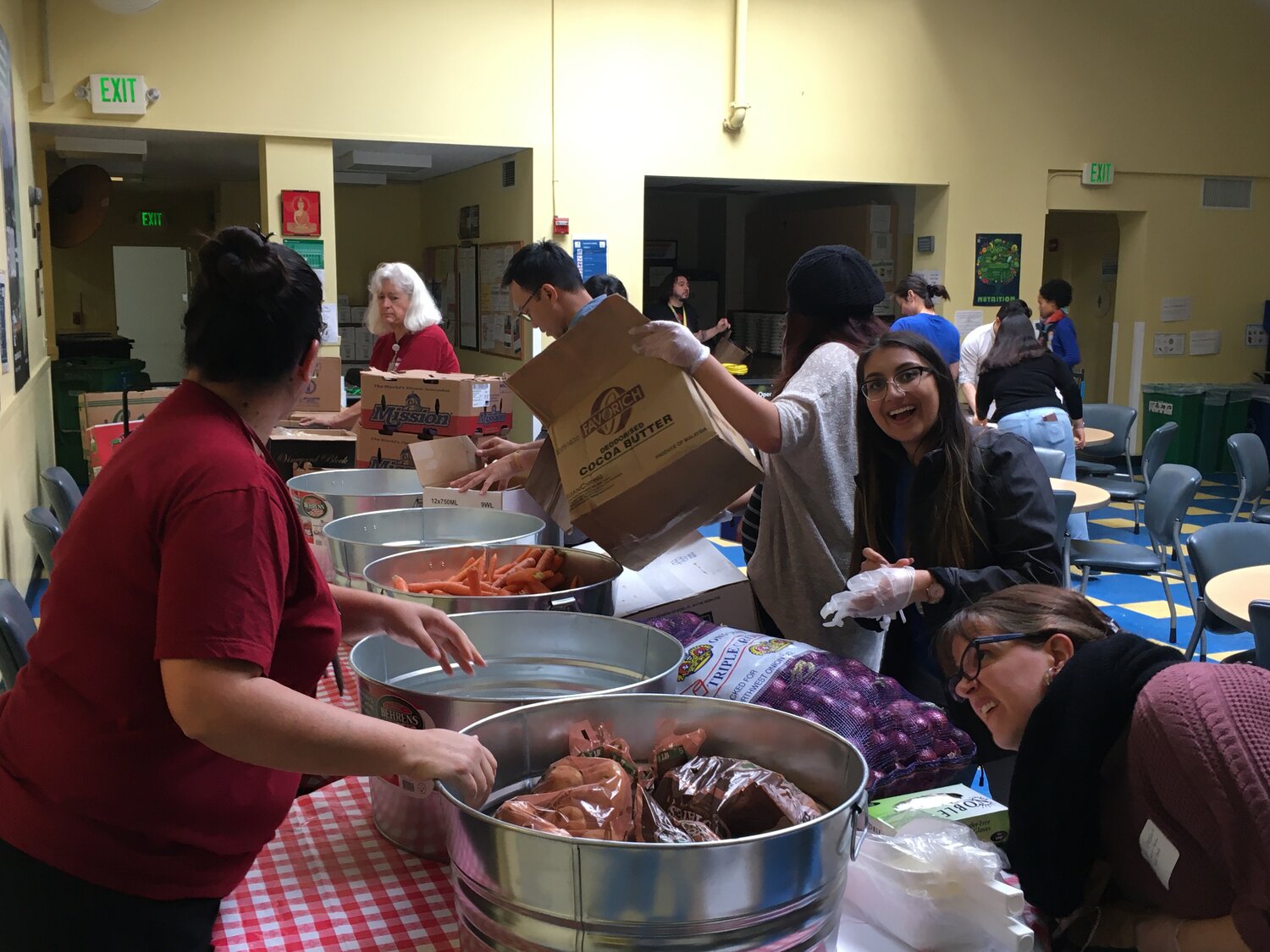 Neha Chhabra smiling behind a table with boxes filled with food to be handed out to seniors at Curry Senior Center.