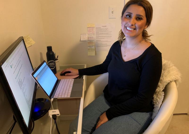 Evelyn De Arcos sitting in a comfy white chair, in front of her computer and monitor, while she serves from home.