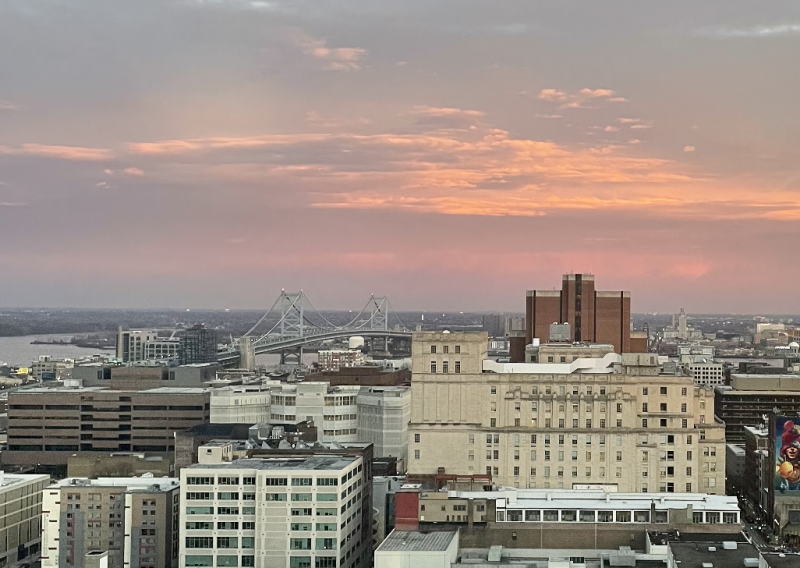 A sunset with buildings and the ben franklin bridge in the foreground