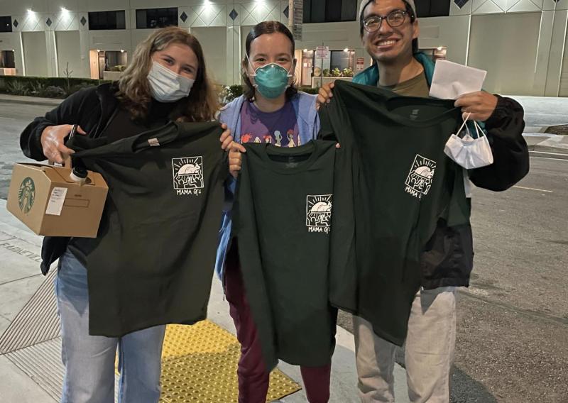 three people stand in the center of the frame, holding up t-shirts 