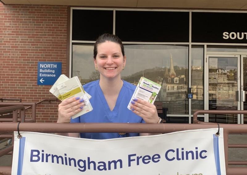 Aurelia is sitting behind a Birmingham Free Clinic sign.