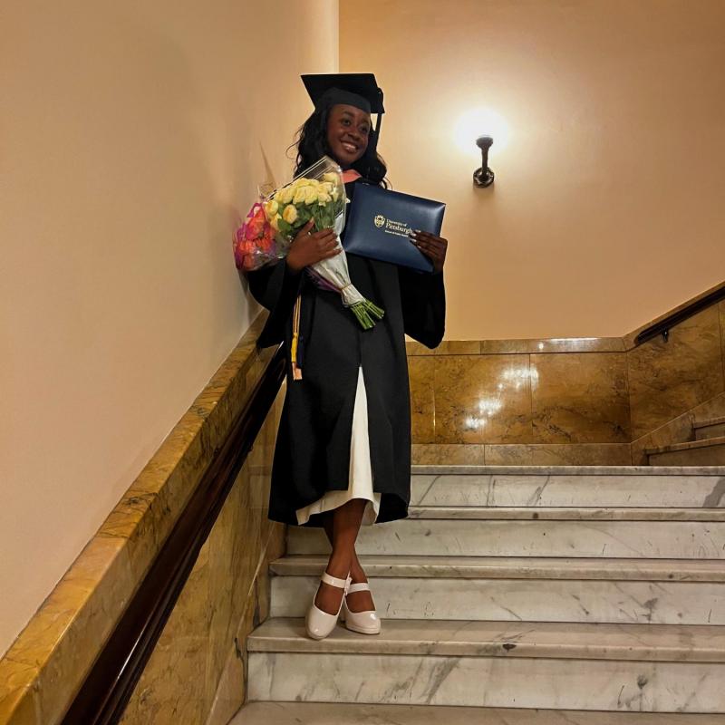 NHC member Chanita Russell wearing graduation attire while holding flowers, diploma, and smiling.