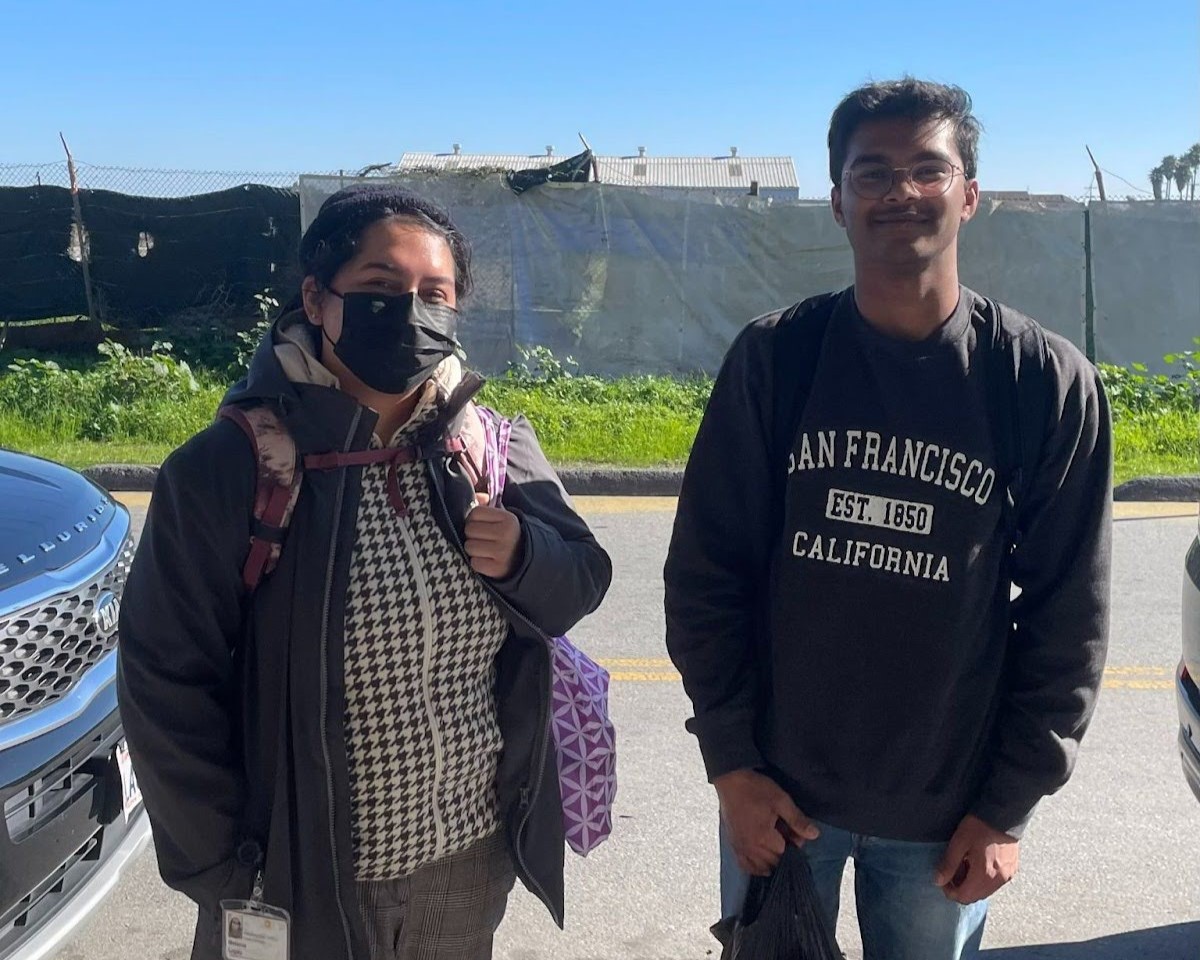 AmeriCorps members Melanie Lopez (left) and Shreyas Raj (right) stand in the center of the frame, facing the camera and smiling. 