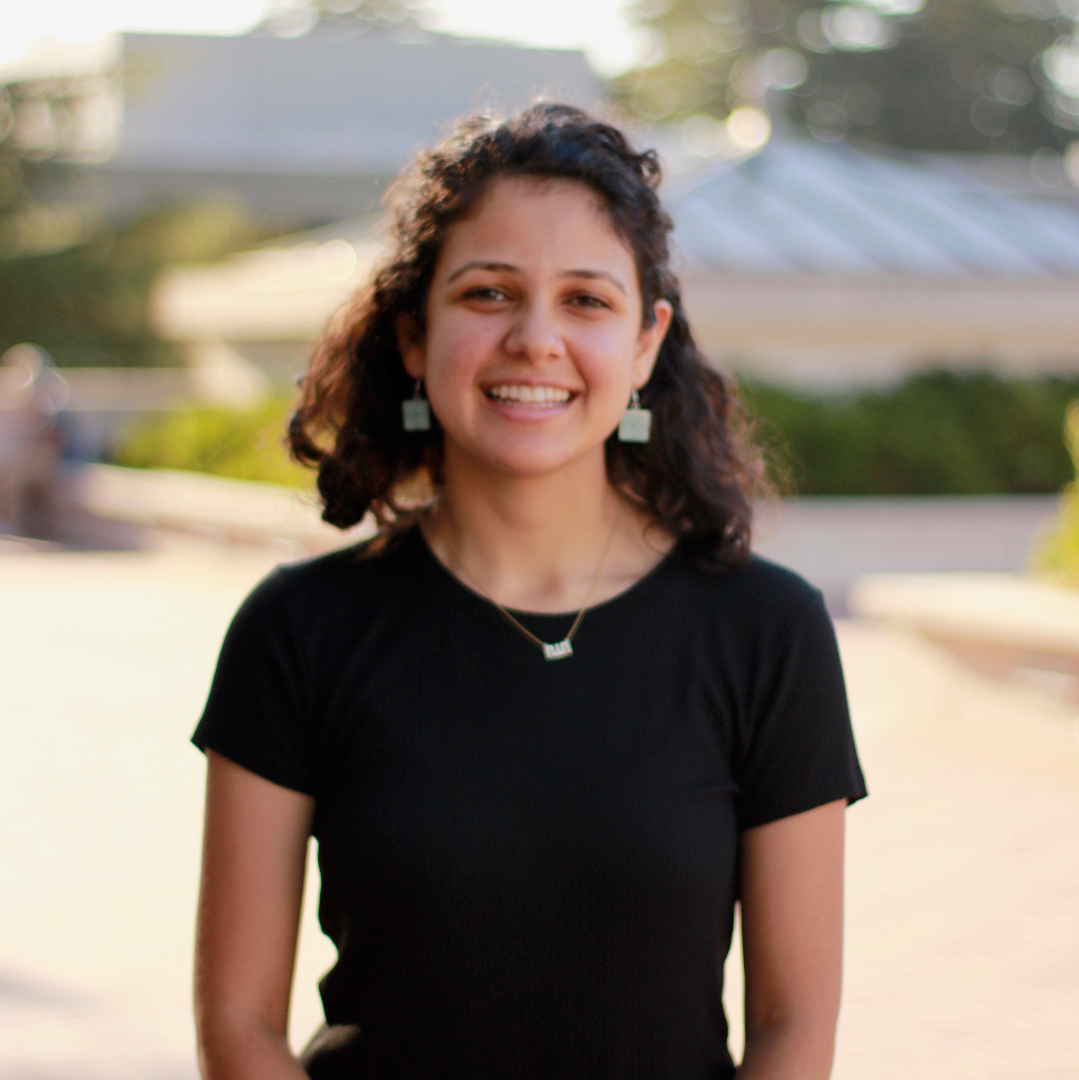 Saba Moussavian is standing in the center of the frame, facing the camera and smiling. 